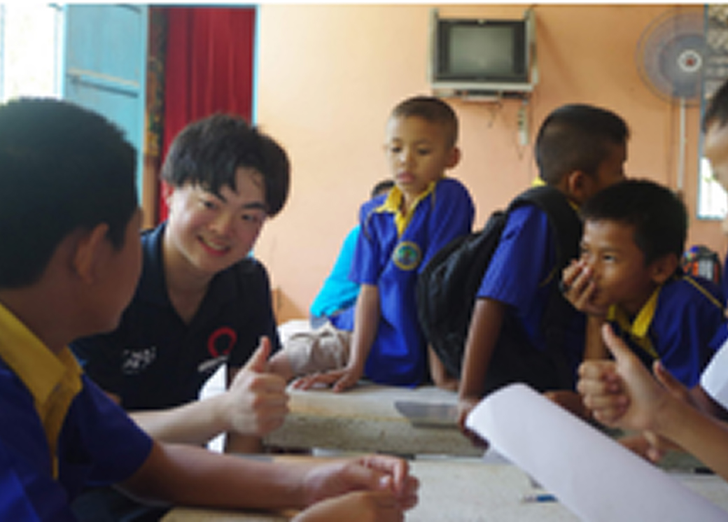 タイの学生たちと日本人参加者が机を囲んで交流している様子。異文化理解や教育活動を行う場面