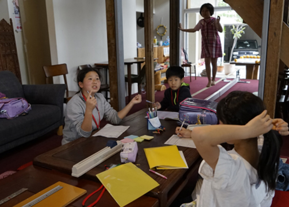 子どもたちと大人がテーブルを囲み、話し合いや作業をしている様子