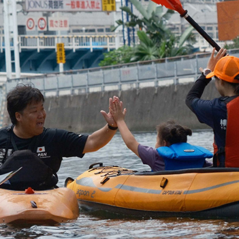 水上で子どもと大人がカヌーに乗り、笑顔で手を振り合っている様子