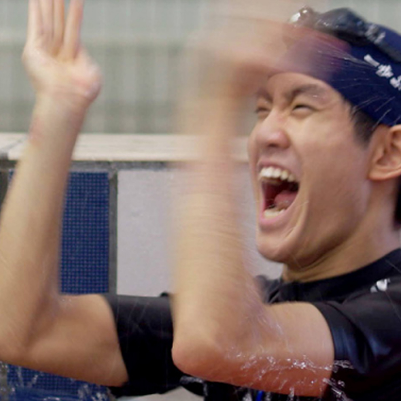 プールで笑顔を見せながら両手を上げて喜ぶ男性の様子。水泳や水中スポーツの体験場面