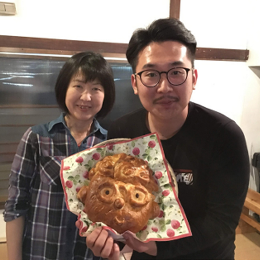 男性と女性が笑顔でカメラに向かい、動物の顔の形をしたパンを手に持っている様子。留学生が日本での料理体験を楽しんでいる