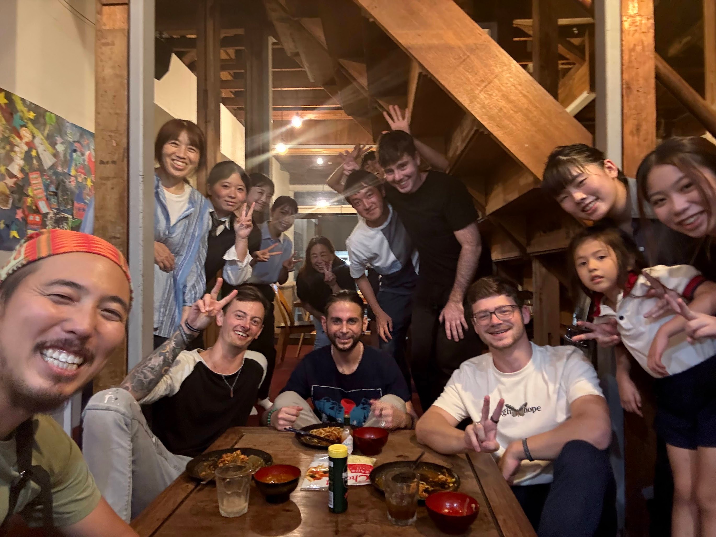 木造建築の室内で、国内外のメンバーが食卓を囲みながら笑顔で集合写真を撮っている様子