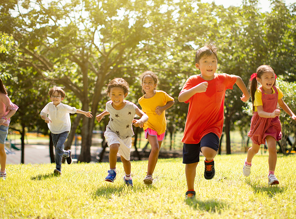 公園の芝生の上を子どもたちが笑顔で元気に走っている様子。明るい日差しの中で友達と一緒に遊び、挑戦する楽しさを感じている