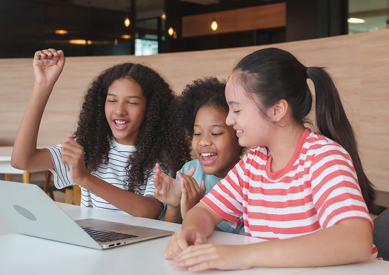 3人の子どもたちがノートパソコンを見ながら笑顔で喜んでいる様子。オンライン学習や協働を表すイメージ